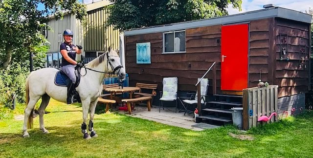 Ruiter te paard naast de pipowagen op het erf