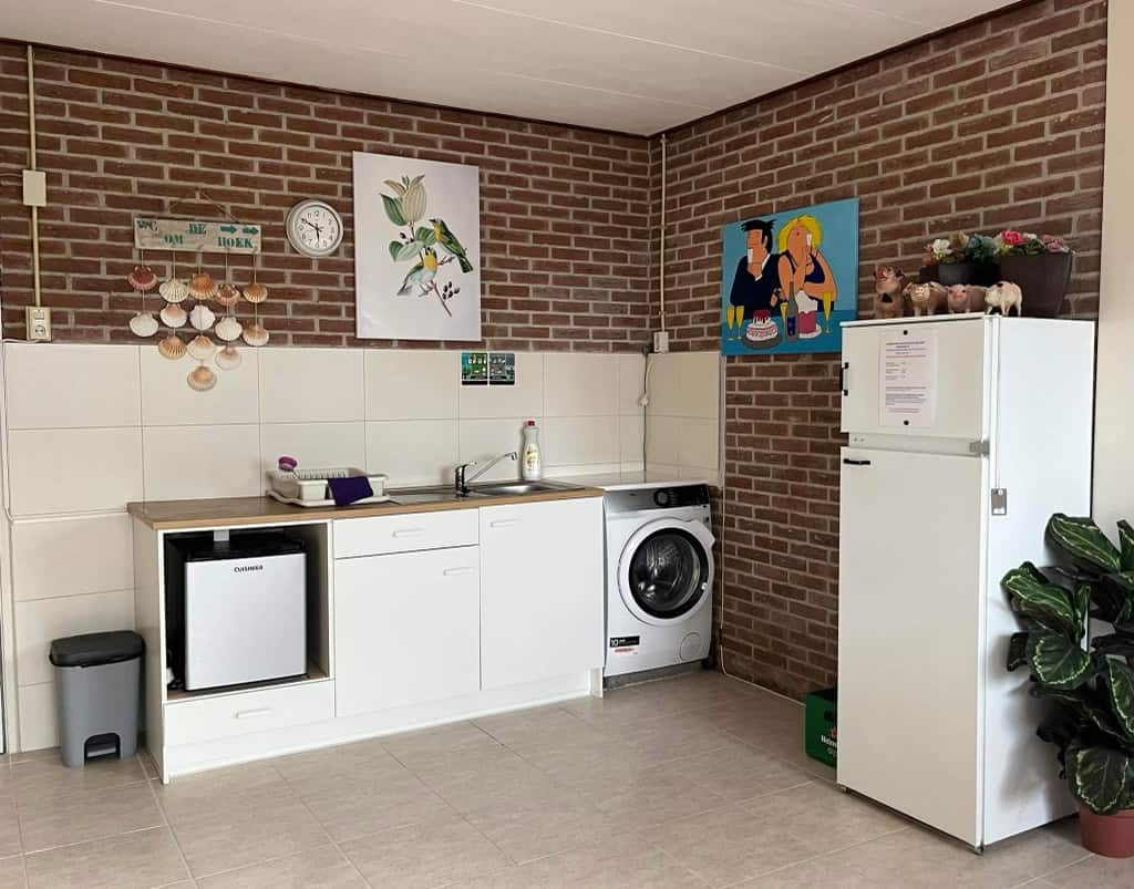 De wasruimte met wasmachine, koelkast en afwasgelegenheid